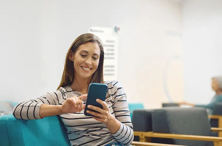 Eine Frau sitzt im Warteraum und scrollt durch ihr Handy (Foto)