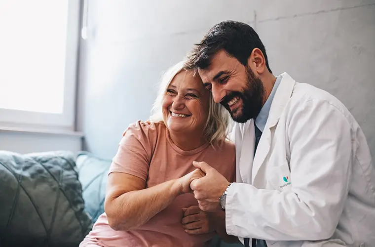 Ein Arzt umarmt eine Patientin und hält ihre Hand, beide lächeln (Foto)
