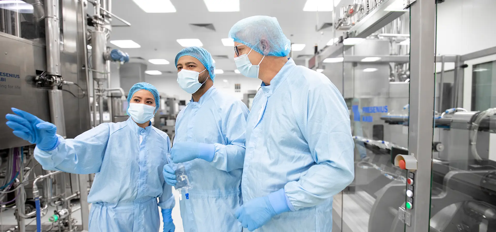 Three employees wearing work clothes and protective masks at a Fresenius production site (Photo)
