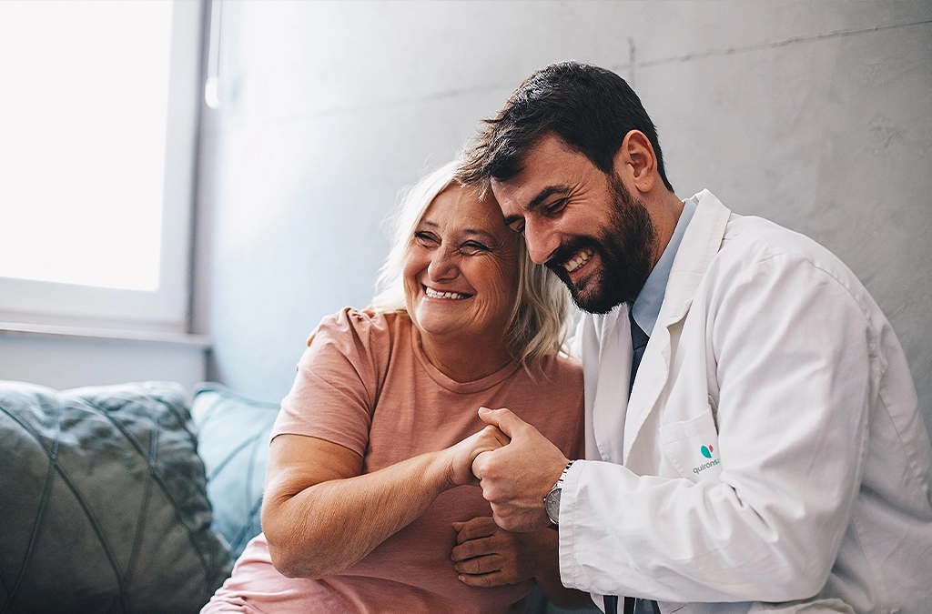 A doctor has his arm around a patient and is holding her hand; both are smiling (Photo)